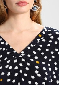 Marineblaues Kleid mit weißen und gelben Punkten, V-Ausschnitt-Design, glatte Stofftextur, mit einem dezenten Glanz.