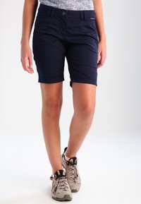 Marinblå shorts med uppvikta fållar, tillverkade av lättviktsmaterial, med framfickor och knäppning. Ett par beige vandringsskor nedanför.