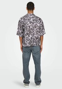 Camisa de manga corta y corte recto con un estampado de leopardo en gris y negro, hecha de una tela suave. Combinada con jeans rectos de mezclilla azul desgastados y zapatillas blancas.