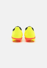 Scarpe da calcio con una tomaia gialla brillante, dettagli neri e una suola rossa. Presentano un design testurizzato e tacchetti sagomati per una migliore aderenza.
