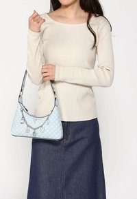 Blauwe gewatteerde handtas met een zilveren ketting en charm-accenten, gecombineerd met een crèmekleurige geribbelde top en een denimrok.