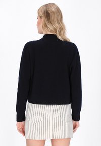 Maglione lavorato a maglia di colore blu navy con design corto e texture a coste, dotato di maniche lunghe e collo alto, abbinato a una gonna a righe.