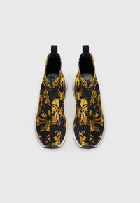 Scarpe slip-on nere con un motivo ornamentale giallo, superiore in tessuto morbido, suola in gomma bianca e linguette nere sul tallone.