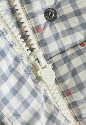 Pilkas ir baltas gingham audinys su mažomis raudonomis dėmėmis, su baltu užtrauktuku, kuris primena meškutį, ir metaliniu spaudimo mygtuku.