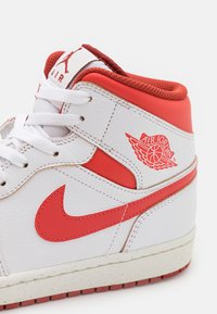 Sneaker alte bianche e rosse in materiale in pelle, con un prominente swoosh rosso di Nike e il logo "Air Jordan" su un lato.