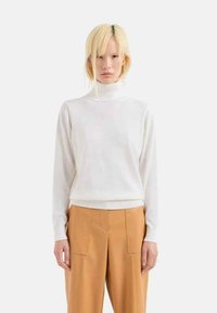 Maglione bianco a collo alto realizzato in un tessuto morbido, con maniche lunghe e orlo a costine, abbinato a pantaloni beige larghi.
