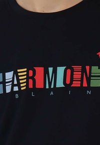 T-shirt nero con testo multicolore che scrive "HARMONY" con motivi variati in rosso, verde, blu e giallo, e "BLAIN" in bianco.