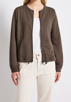 Gewatteerd bruin jack met een ronde hals, ritssluiting, zijzakken en geribbelde manchetten. Gecombineerd met crèmekleurige broek.