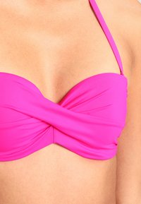 Růžový bikiny top s bandeau designem, s překrouceným předním detailem a tenkými nastavitelnými ramínky. Hladký, elastický materiál.