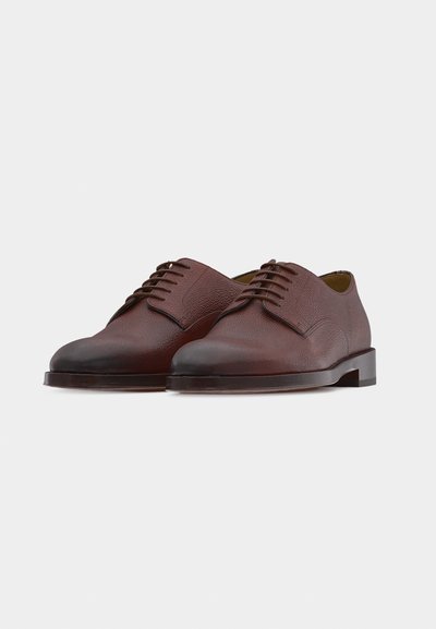 Paire de chaussures habillées en cuir marron à lacets, bouts arrondis et finition texturée sur fond blanc.