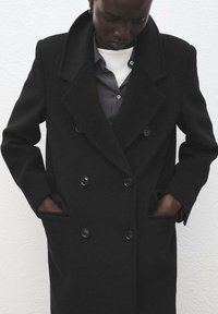 Czarny dwurzędowy płaszcz z mieszanki wełny, z szerokim kołnierzem, dużymi guzikami i bocznymi kieszeniami, zaprojektowany na dopasowany krój.