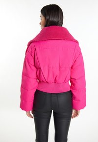 Giacca puffer in corduroy rosa con un colletto oversized texturizzato e vita a coste. Abbinata a pantaloni neri aderenti.