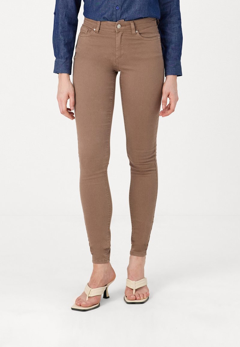 Jeans slim fit marron en denim extensible, dotés d'une taille haute et de poches avant, associés à des escarpins à bout ouvert de couleur claire.
