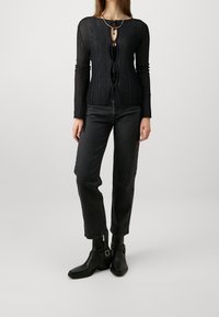 Svart ribbad långärmad topp med nyckelhålsknäppning, framsnörning och kontrasterande textur, matchad med svarta raka jeans och svarta ankelstövlar.