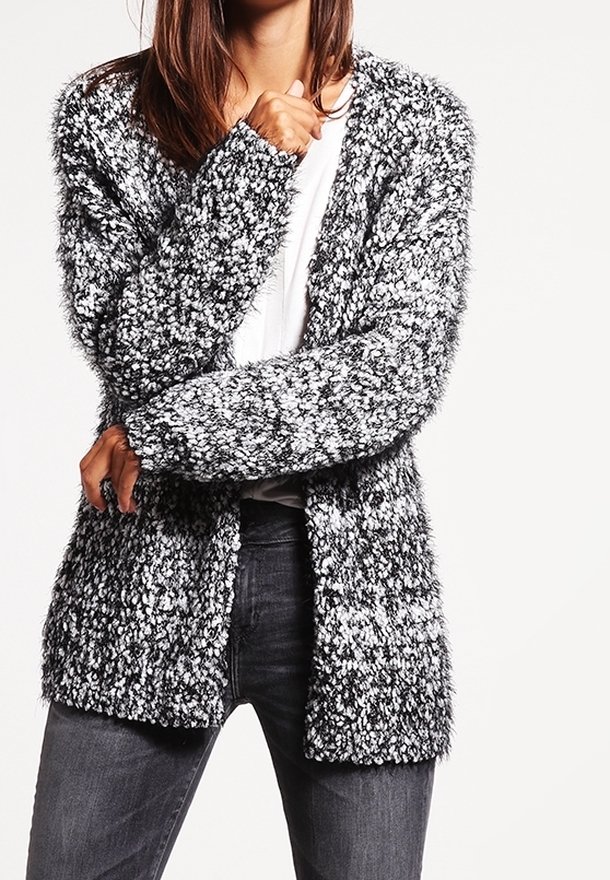 Texturerad svartvit cardigan med lös passform, öppen front och långa ärmar, tillverkad av mjukt och lurvigt material. Bärs över en vit topp.