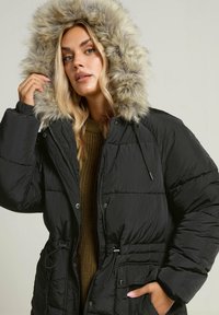 Czarna kurtka puchowa z odpinanym kapturem z sztucznego futra, z zapięciem na zamek, ściągaczem w talii i pikowaną fakturą.