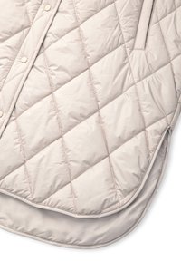 Přikrývkový bežový svrchní oděv s hladkou texturou, diagonálním prošíváním a patentkami, s bočními kapsami.