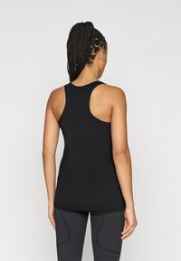 Musta tankkitoppi racerback-mallilla, tehty sileästä, joustavasta kankaasta. Siinä on pyöristetty helma ja saumadetaljit, jotka antavat istuvan ilmeen.