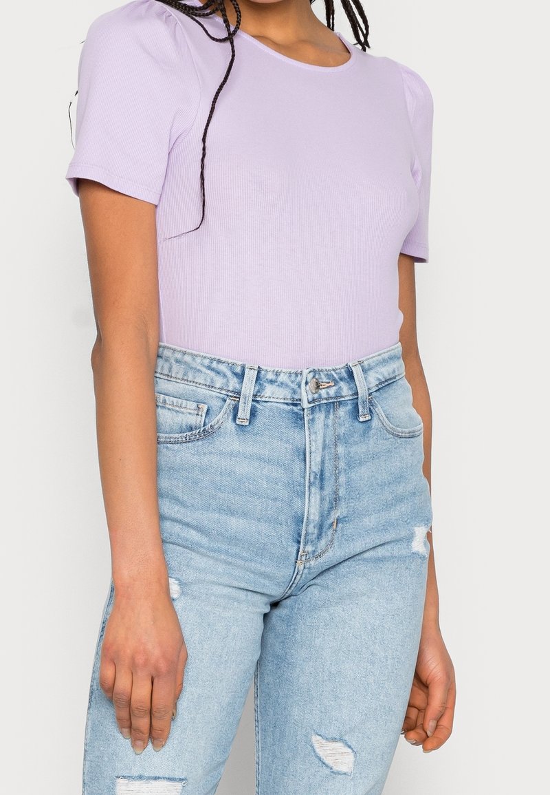 T-shirt lilas à rayures avec des manches courtes, associé à un jean en denim bleu clair déchiré taille haute, avec cinq poches et une fermeture éclair.