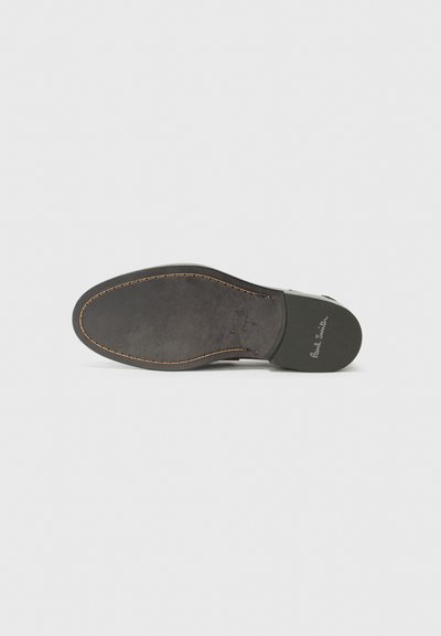 Semelle d'une chaussure avec un fond en caoutchouc noir, présentant une texture lisse et des détails cousus, arborant le nom de la marque "Paul Smith."