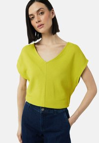 Żółta, prążkowana bluzka z krótkim rękawem i dekoltem w kształcie V, w połączeniu z ciemnoniebieskimi dżinsami. Charakteryzuje się luźnym krojem i subtelną teksturą.