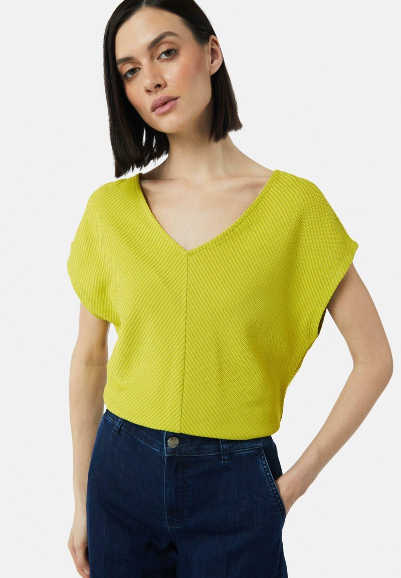Żółta, prążkowana bluzka z krótkim rękawem i dekoltem w kształcie V, w połączeniu z ciemnoniebieskimi dżinsami. Charakteryzuje się luźnym krojem i subtelną teksturą.
