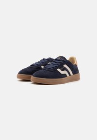 Pair of dark blue suede sneakers with beige accents, white side stripes, gum soles, and blue laces on a plain white background.