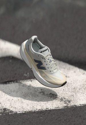 Chaussure de course New Balance avec une tige en maille gris clair, une semelle intermédiaire crème, des accents gris foncé et un design élégant et aérodynamique.