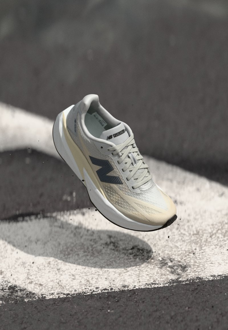 Chaussure de course New Balance avec une tige en maille gris clair, une semelle intermédiaire crème, des accents gris foncé et un design élégant et aérodynamique.