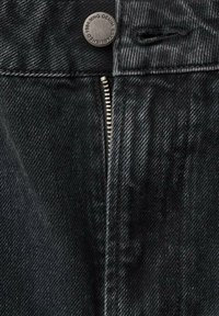 Jean en denim noir avec un bouton en métal et une braguette zippée. La texture présente un motif sergé subtil avec une finition légèrement délavée.