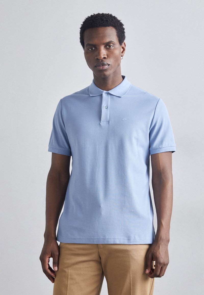 Light blue polo shirt made of cotton, featuring a collar, short sleeves, and a subtle logo on the chest. Smooth texture, classic fit.