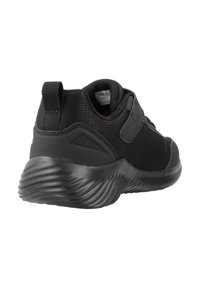 Zapatilla deportiva negra con un upper de malla texturizada, correa de velcro y suela acolchada con patrones ondulados. Diseño duradero adecuado para un uso activo.