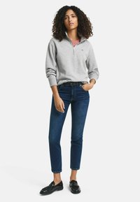 Grijze sweatshirt met rits en hoge kraag, gecombineerd met donkerblauwe slim-fit jeans en zwarte loafers. Zachte stof, casual ontwerp en aansluitende stijl.