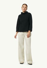 Top nero con collo a cowl e un motivo a spina di pesce testurizzato, abbinato a pantaloni cream a gamba larga. L'outfit presenta una vestibilità comoda e maniche lunghe.