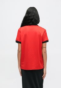 Czerwona koszula z krótkim rękawem o gładkiej fakturze, z czarnym kołnierzykiem i mankietami. Wzór zawiera pionowe paski na tkaninie.