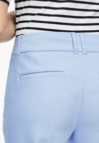 Světlé modré kalhoty mají na zadní straně plochou kapsu, vyrobené z hladké látky, která doplňuje černobíle pruhovaný top nahoře.