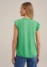 Top verde a maniche corte con accenti di spalle arricciate e scollatura rotonda, realizzato in tessuto leggero, con orlo curvo.
