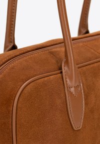 Borsa a mano in suede marrone con manici in pelle liscia, cuciture dettagliate e una forma strutturata con chiusura a zip.