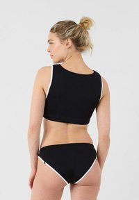 Reggiseno sportivo nero e bikini abbinato in materiale a asciugatura rapida, con bordo bianco, design elegante e forma aderente. Mostrata la vista posteriore.