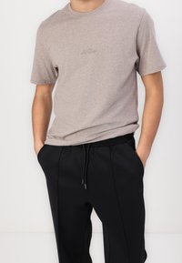 Hellbraunes T-Shirt mit kurzen Ärmeln und rundem Ausschnitt, kombiniert mit schwarzen Jogginghosen mit verstellbarem Kordelzug und Seitentaschen.