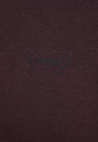 Tissu en tricot violet foncé avec un petit logo noir "hummel" centré à l'intérieur d'un triangle arrondi irrégulier.