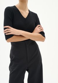 Top tricotat negru cu dungi, cu decolteu în V și mâneci scurte, combinat cu pantaloni negri cu talie înaltă. Textură netedă, design ajustat.