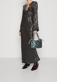 Lång svart klänning med ett virvlande mönster, nyckelhalsringning, flödande ärmar. I kombination med en liten blå satinhandväska och bruna blockklackstövlar.