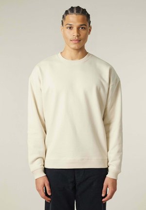Felpa leggera beige chiaro con colletto a giro e maniche lunghe, polsini e orlo a costine. Materiale in cotone, vestibilità rilassata, design minimalista.