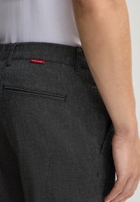 Pantaloni grigi con fantasia e tessuto testurizzato, dotati di una tasca posterior e di un piccolo etichetta rossa "JOOP! JEANS" in vita.
