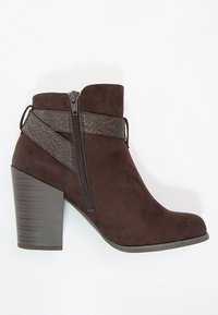 Bota de tobillo de ante marrón con una correa texturizada de color marrón oscuro, cremallera lateral y un tacón grueso apilado. Presenta un diseño de puntera lisa.