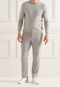 Maglione grigio chiaro e pantaloni abbinati realizzati in un tessuto morbido. Caratterizzati da un collo rotondo, maniche lunghe e una vestibilità slim, abbinati a scarpe da ginnastica bianche.