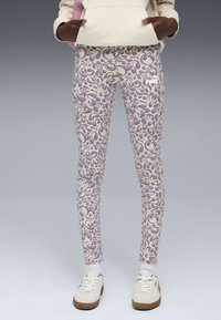 Leggings de couleur crème avec un motif abstrait fantaisiste en violet et rose. Ils offrent un ajustement près du corps et un subtil logo sur la cuisse.