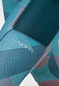 Patroond leggings met een mix van teal, marineblauw en koraal kleuren, met mesh accenten, een gladde textuur en een logo aan de zijkant.