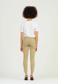 Beige fitted broek met achterzakken, gedragen met een wit T-shirt, weergegeven van de achterkant. Hoge zwarte sandalen zichtbaar.